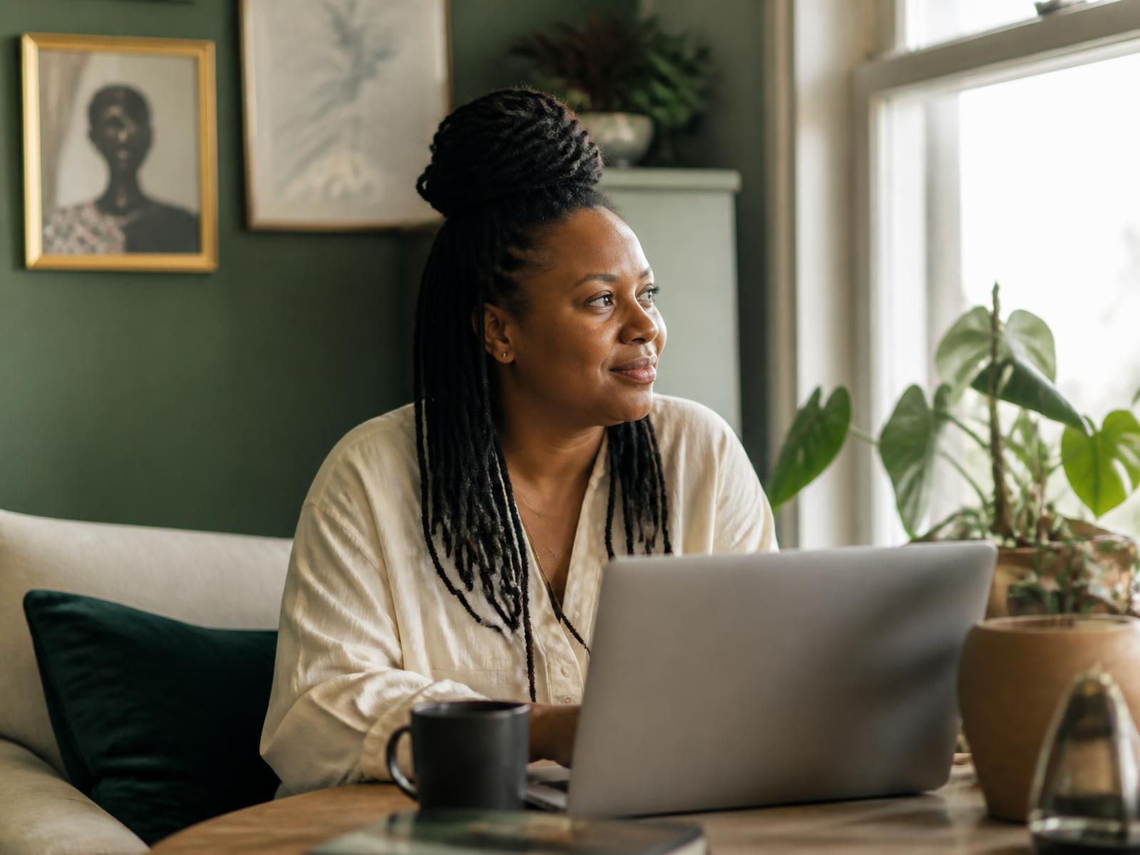 A woman at home joining a telehealth therapy session on her laptop by a sunlit window